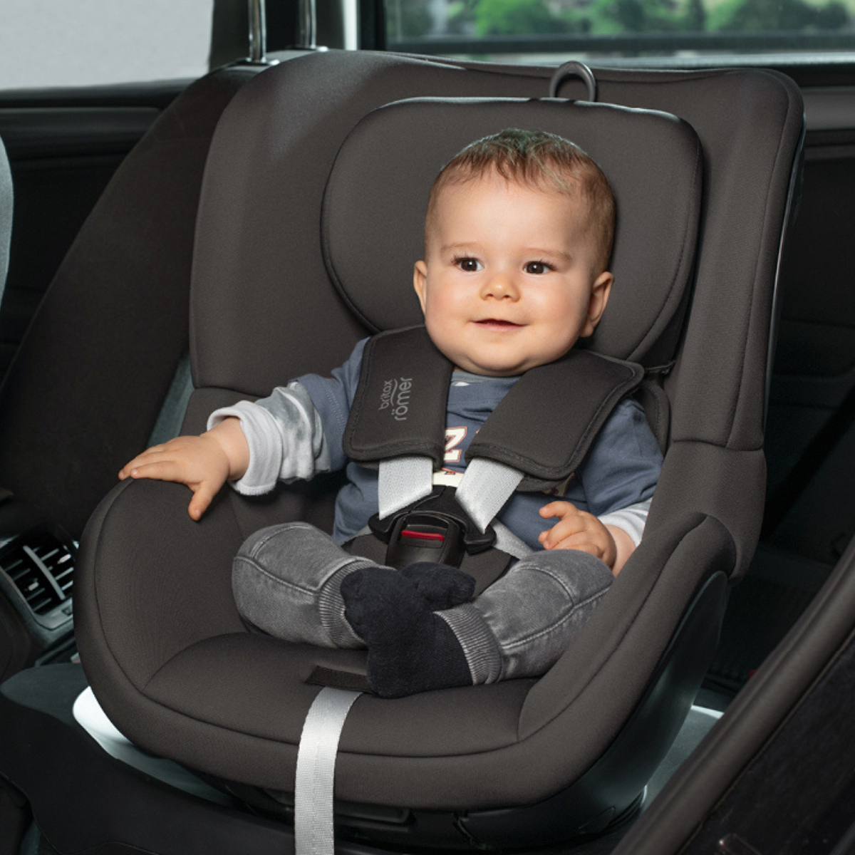 Child secured in a SWINGFIX M PLUS car seat inside a car.